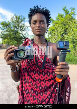 Un giovane guerriero Maasai possiede una videocamera GoPro 11 e una fotocamera digitale Leica M10-R nel suo villaggio di Mikumi, Tanzania. Foto Stock