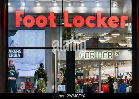 Attraverso una vista in vetro degli addetti agli acquisti in piedi vicino ai prodotti nello showroom illuminato, con cartello Foot Locker esposto sulla parete in vetro Foto Stock