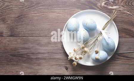 Uova di Pasqua dipinte di blu con macchie dorate e alcuni fiori secchi su un piatto con fiori su sfondo in legno e spazio per copiare. Foto Stock