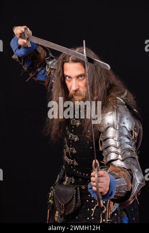 Composizione verticale. Ritratto di un uomo carismatico vestito da cavaliere medievale con due spade durante una rievocazione storica. Foto Stock