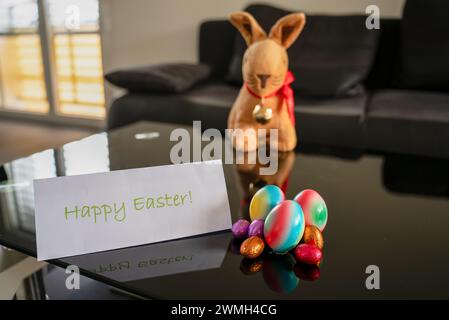 Gruppo di uova di pasqua di diverse dimensioni e colori sul tavolo con spigolo di pasqua sfocato sullo sfondo e cartolina di Pasqua felice in primo piano. Foto Stock