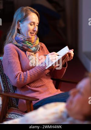 Una psicologa donna adulta intervista una paziente e prende appunti in un quaderno. Composizione verticale. Foto Stock