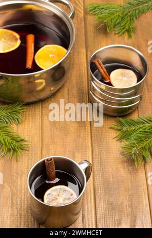 VIN brulé agli agrumi con spezie in tazze metalliche e pentola. Anice stellato, zeppe arancioni e cannella sul tavolo. Sfondo in legno. Foto Stock