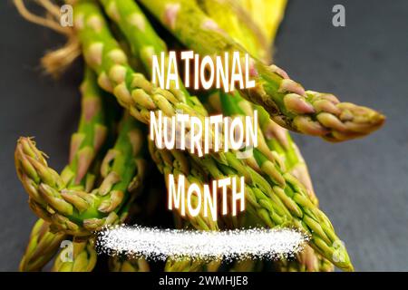 National Nutrition Month, con un pacchetto di asparagi freschi legati con spago su una lavagna di ardesia, accompagnati da testo colorato. Foto Stock