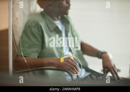 Ripresa laterale ritagliata di un uomo nero adulto che indossa un berretto mentre riceve un trattamento IV dietro un vetro nello spazio di copia della clinica Foto Stock