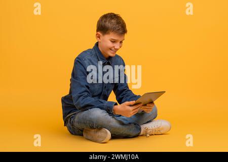 Adolescente che usa un tablet digitale seduto a gambe incrociate per terra in studio Foto Stock