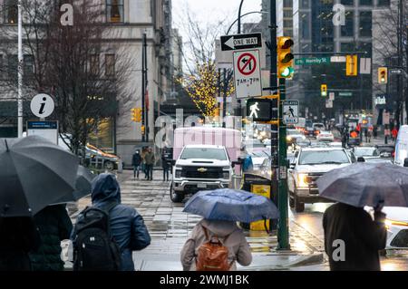 Persone in attesa del cartello pedonale per attraversare Howe Street in un giorno di pioggia, tenendo in mano gli ombrelli, di fronte alla piazza della Vancouver Art Gallery. Foto Stock