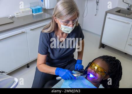 Dentista donna che esegue il restauro dei denti con lampada di riempimento e polimerizzazione per paziente femminile] Foto Stock