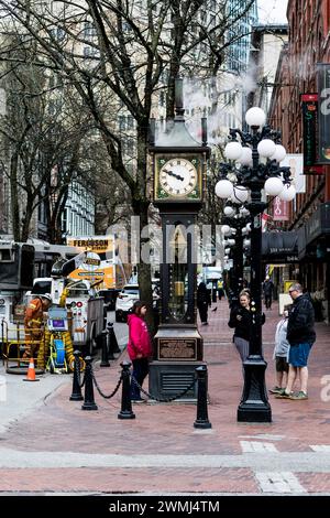 Una vista dell'Orologio a vapore di Gastown, con il vapore che esce dalla sua parte superiore e i dettagli del suo volto, e una famiglia di turisti che lo guardano. Foto Stock