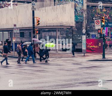 Vancouver, Canada - 21 febbraio 2024: Persone che attraversano Howe Street, tenendo i loro ombrelli, con la Galleria d'Arte visibile sullo sfondo. Foto Stock