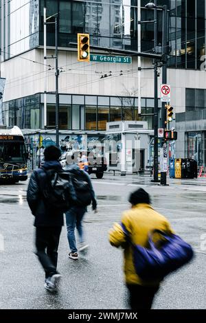 Vancouver, Canada - 21 febbraio 2024: Persone che attraversano Georgia Street al semaforo. La bassa velocità dell'otturatore ha offuscato il loro movimento. Foto Stock