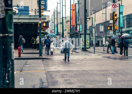 Vancouver, Canada - 21 febbraio 2024: Una persona che attraversa Georgia Street al semaforo, indossa un poncho impermeabile trasparente monouso. Foto Stock