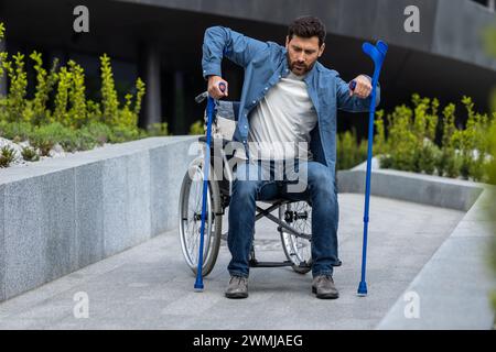 Giovane barbuto con bastoni su una sedia a rotelle Foto Stock