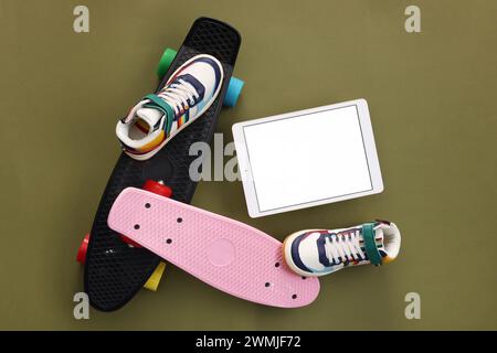Tablet moderno, skateboard e scarpe su sfondo verde oliva, piatto. Spazio per il testo Foto Stock