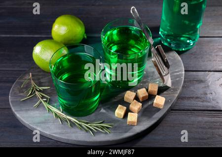 Assenzio in bicchieri, rosmarino, zucchero di canna e calce su un tavolo di legno. Bevanda alcolica Foto Stock