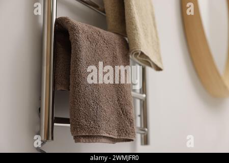 Portasciugamani riscaldato con asciugamani marroni in bagno, primo piano Foto Stock