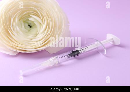 Cosmetologia. Siringa medica e fiore ranunculus su sfondo viola, primo piano Foto Stock