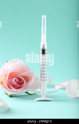 Cosmetologia. Siringa medica, fiore di rosa e petali su sfondo turchese Foto Stock