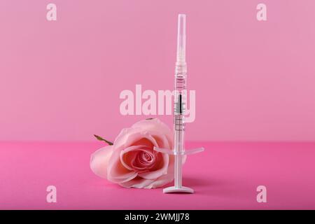 Cosmetologia. Siringa medica e fiore di rosa su sfondo rosa Foto Stock