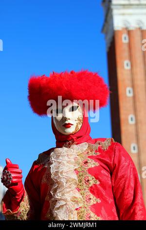Persona mascherata con volto coperto da maschera e ampio copricapo durante il carnevale di Venezia con il campanile di San Marco sullo sfondo Foto Stock