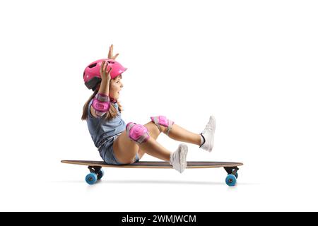 Foto a tutta lunghezza di una bambina seduta su uno skateboard e che cavalca isolata su sfondo bianco Foto Stock