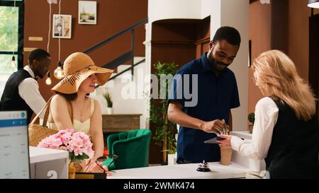 Gli ospiti dell'hotel effettuano il check-in alla reception, firmando documenti elettronici su tablet. I viaggiatori alla reception compilano i documenti di registrazione per la prenotazione delle camere durante le vacanze estive al mare. Scatto a mano libera. Foto Stock