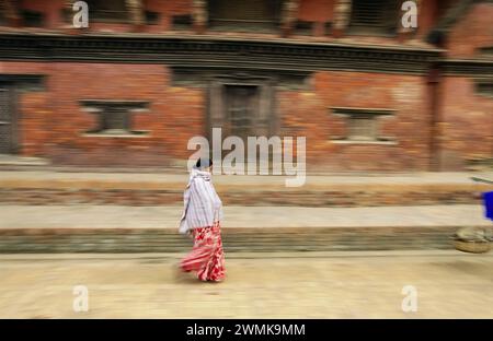 Vista panoramica di una donna nepalese che si precipita davanti a un edificio in mattoni; Kathmandu, Nepal Foto Stock