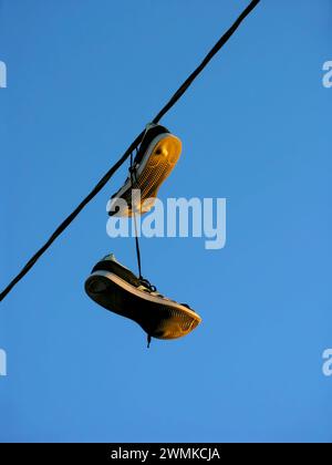 Scarpe che penzolano da un cavo sospeso contro un cielo blu Foto Stock