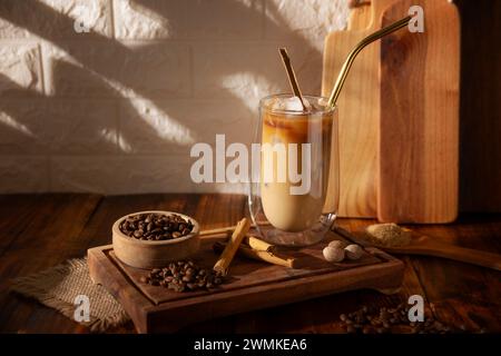 Caffè freddo servito in una tazza di vetro a doppia parete e paglia di metallo, una bevanda estiva fredda preparata con cubetti di ghiaccio e spezie, cannella, noce moscata, vaniglia, mu Foto Stock