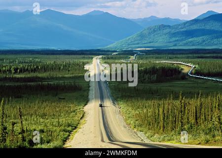 Un camion solitario si sposta lungo la Dalton Highway (conosciuta anche come Haul Road) attraverso la tundra verde con una vista spettacolare verso le montagne, correndo 414 ... Foto Stock