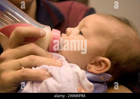 La bambina di 2 1/2 mesi si fa forare le orecchie in un centro commerciale e viene calmata da un biberon: Lincoln, Nebraska, Stati Uniti d'America Foto Stock