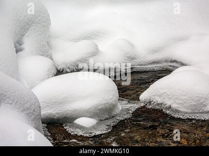 Primo piano di rocce innevate lungo un ruscello aperto; Lake Louise, Alberta, Canada Foto Stock