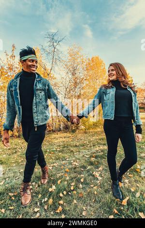 Coppia di sposi con corse miste sorridenti, camminando in un parco cittadino durante un'uscita di famiglia autunnale, trascorrendo del tempo di qualità insieme Foto Stock