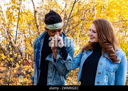 Una coppia di sposi di razza mista che cammina insieme durante una gita di famiglia autunnale in un parco cittadino mentre il marito bacia la mano di sua moglie: Edmonton, Alberta, Canada Foto Stock