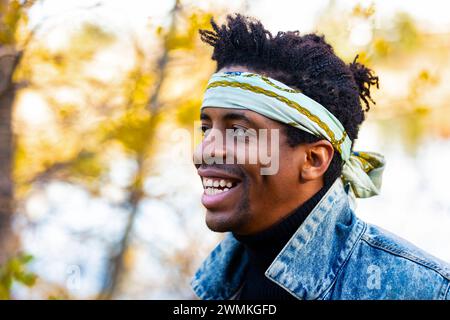 Ritratto ravvicinato di un bell'uomo che indossa un cerchietto di bandanna, sorridente in un parco cittadino in autunno; Edmonton, Alberta, Canada Foto Stock