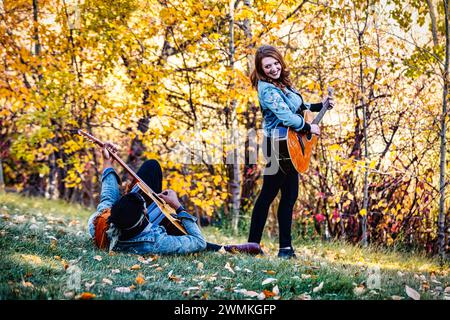 Coppia di sposi in gara mista che trascorrono del tempo insieme, sorridendo e suonando le chitarre durante una gita in famiglia autunnale in un parco cittadino Foto Stock