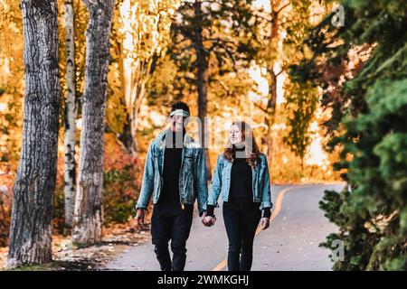 Una coppia di sposi che cammina lungo una strada in un parco cittadino durante un'uscita di famiglia autunnale, tenendosi per mano, trascorrendo del tempo insieme Foto Stock