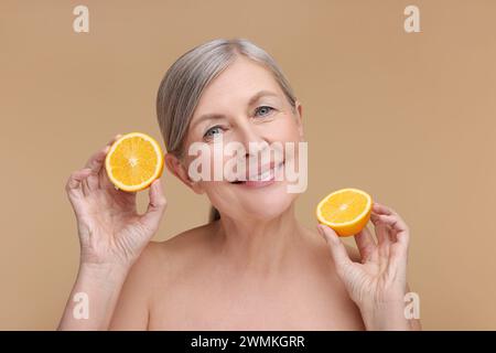 Bella donna con metà di arancia ricca di vitamina C su sfondo beige Foto Stock