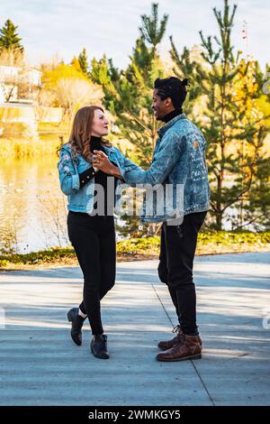 Una coppia di corse miste che ballano e si divertono mentre trascorrono del tempo insieme durante una gita in famiglia autunnale in un parco cittadino: Edmonton, Alberta, Canada Foto Stock