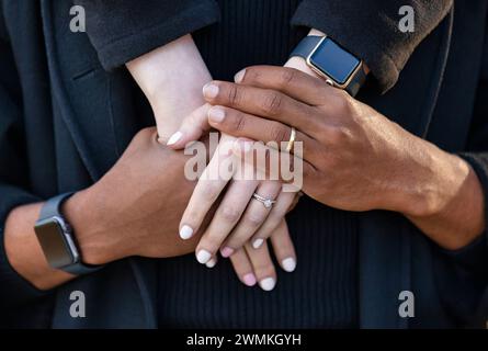 Primo piano delle mani interchiuse di una coppia di corse miste, trascorrendo del tempo insieme durante una gita in famiglia autunnale in un parco cittadino Foto Stock