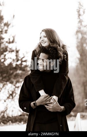 Ritratto in bianco e nero di una coppia mista, moglie che abbraccia il marito da dietro, mentre trascorre del tempo insieme durante una famiglia autunnale... Foto Stock