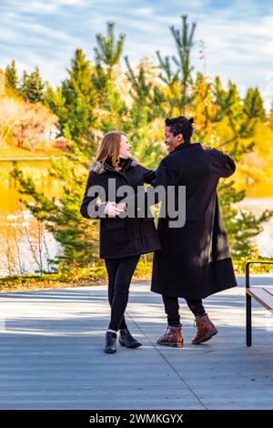 Una coppia di corse miste che ballano e si divertono mentre trascorrono del tempo insieme durante una gita in famiglia autunnale in un parco cittadino: Edmonton, Alberta, Canada Foto Stock