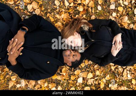 Una coppia di corse miste stesa a terra in autunno se ne va, guardandosi faccia a faccia, mentre trascorreva del tempo insieme durante un autunno del ... Foto Stock