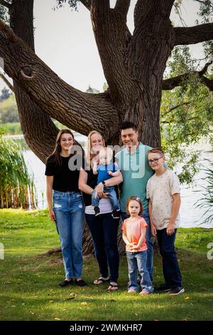 Ritratto di famiglia all'aperto in un parco cittadino vicino a un lago in un caldo pomeriggio autunnale e il figlio più giovane ha la sindrome di Down; Leduc, Alberta, Canada Foto Stock