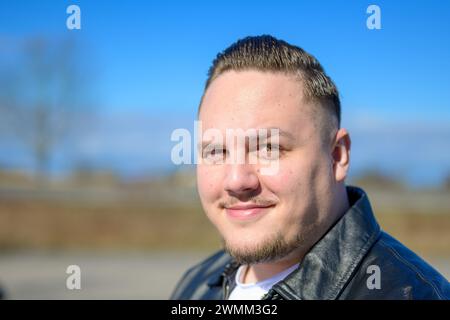 Un giovane uomo attraente di vent'anni si trova fuori in un parco in primavera e guarda la macchina fotografica Foto Stock