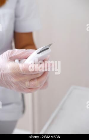 Primo piano delle mani dell'estetista con guanti con dispositivo professionale per la pulizia del viso a ultrasuoni, pronto per la cura della pelle. Foto verticale Foto Stock