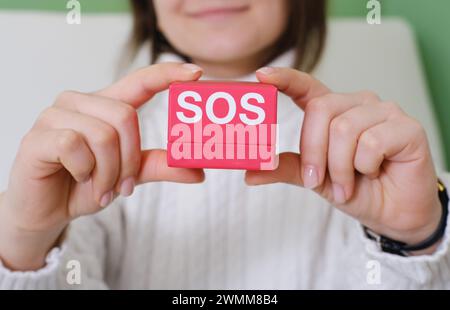 Mani che presentano un piccolo pacchetto rosso di crema per la pelle SOS, che simboleggia il trattamento e il sollievo urgenti per la cura della pelle Foto Stock