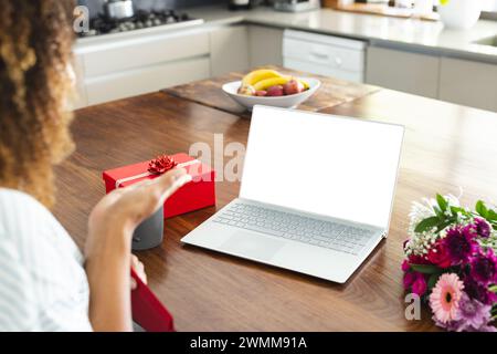 Una donna birazziale gode di un regalo a sorpresa a casa durante una videochiamata online con spazio di copia Foto Stock