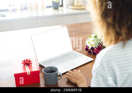 Una donna birazziale ama un appuntamento online accogliente con regali e fiori a casa. Foto Stock