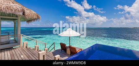 Lussuoso resort sulla spiaggia, bungalow vicino a una piscina infinita su un bellissimo mare blu. Incredibile isola tropicale, concetto di vacanza estiva. Coppia di sedie con ombrello Foto Stock